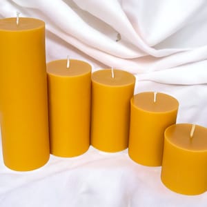 May include: Five beeswax candles of varying sizes, arranged in a row from largest to smallest. The candles are a warm, golden yellow color.