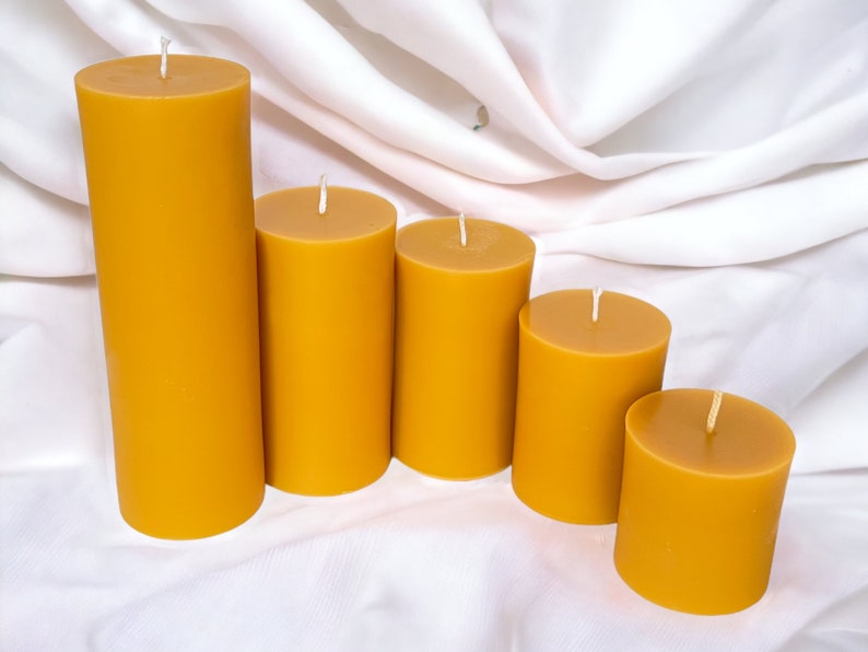 May include: Five beeswax candles of varying sizes, arranged in a row from largest to smallest. The candles are a warm, golden yellow color.