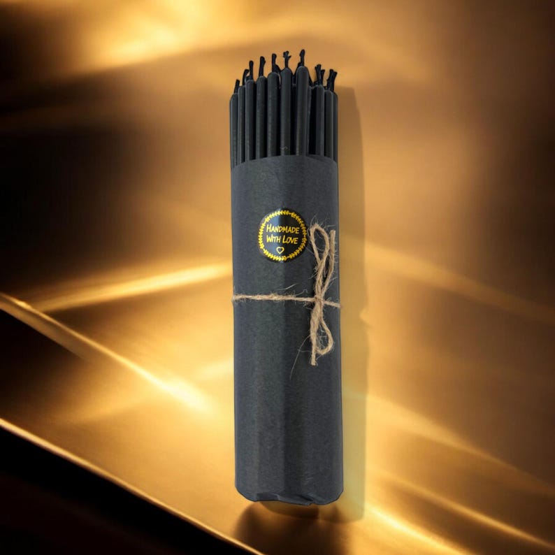 May include: A bundle of black birthday candles wrapped in black paper with a gold sticker that says "Handmade with Love".