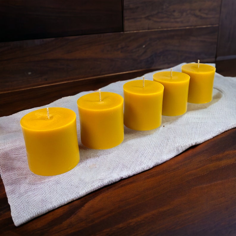 May include: Five yellow pillar candles on a white cloth surface. The candles are arranged in a row, with the largest candle at the back and the smallest candle at the front.