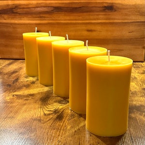 May include: Four yellow beeswax candles arranged in a row on a wooden surface. The candles are all the same size and shape, and they have a natural, rustic look.