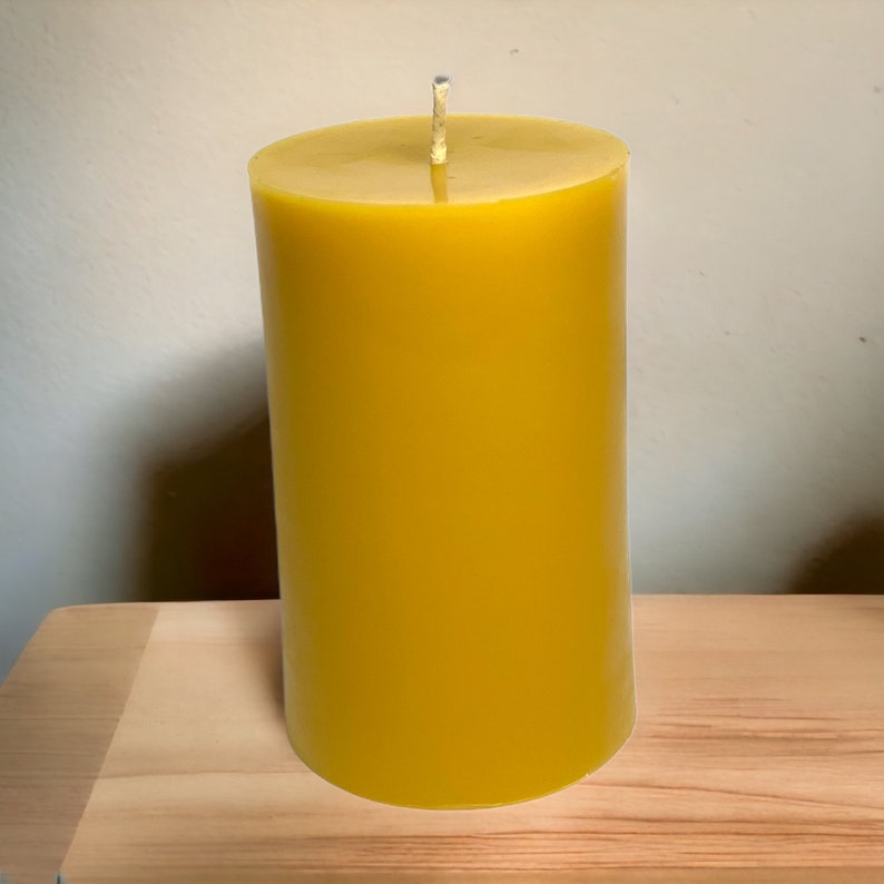 May include: A large, cylindrical, yellow beeswax candle with a white wick.