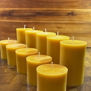 May include: A group of ten round, golden yellow beeswax candles arranged in a row on a wooden surface. The candles are all the same size and have a white wick.
