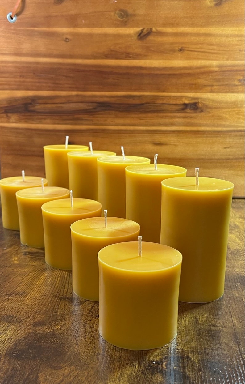 May include: A group of ten round, golden yellow beeswax candles arranged in a row on a wooden surface. The candles are all the same size and have a white wick.