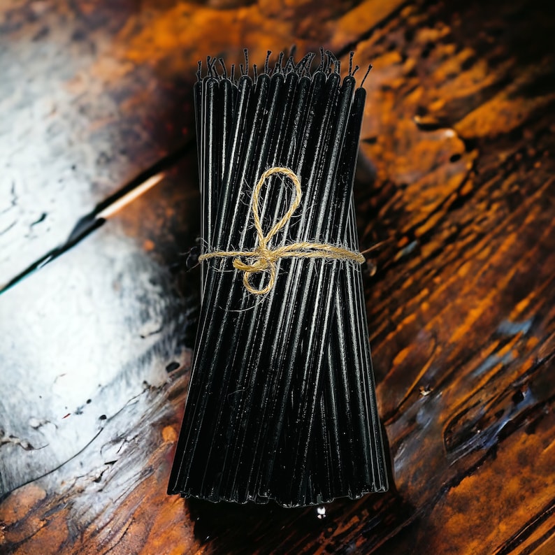 May include: A bundle of black taper candles tied together with twine. The candles are arranged in a neat stack and are ready to be used.