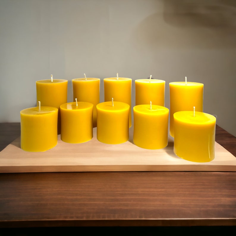 May include: Ten yellow beeswax candles arranged in a row on a wooden surface. The candles are all the same size and shape, and they are all lit.