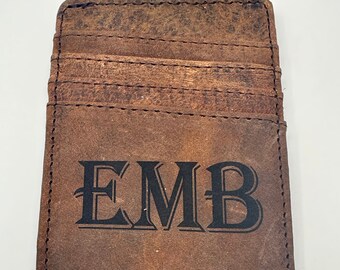 May include: A brown leather wallet with a money clip and three card slots. The wallet has the initials "EMB" embossed on the front.