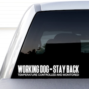 May include: A white decal with black text that reads "Working Dog - Stay Back" and "Temperature Controlled and Monitored" on a black car window.
