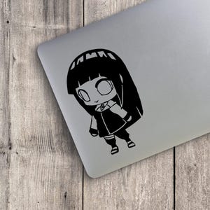 May include: A black vinyl decal featuring a stylized chibi-style anime character with long straight hair, large eyes, and a layered outfit. The character is depicted in a standing pose with a small emblem on the chest area, rendered in solid black.
