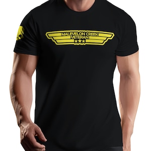 May include: A black short-sleeve t-shirt featuring a yellow graphic on the chest with the text MALEVELON CREEK VETERAN and three stars inside a winged emblem. A small yellow skull icon is printed on the right sleeve of the garment.
