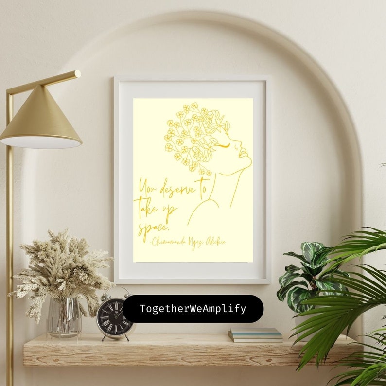 May include: A yellow and white printable art print with a line drawing of a woman with flowers in her hair. The quote "You deserve to take up space." is written in gold lettering with the author "Chimamanda Ngozi Adichie" below. The print is framed and hanging on a wall.