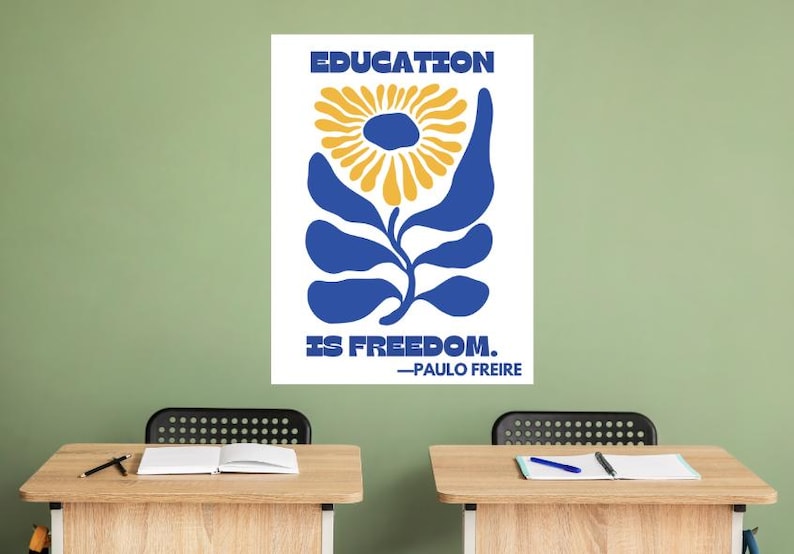 Pu&ograve; includere: Un poster bianco con illustrazioni blu e gialle di un fiore. Il poster recita "EDUCATION IS FREEDOM. -PAULO FREIRE".