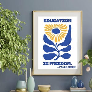 Pu&ograve; includere: Una stampa incorniciata con uno sfondo bianco e un fiore stilizzato blu con un centro giallo. Il testo "EDUCATION IS FREEDOM." &egrave; stampato sotto il fiore, con la citazione "PAULO FREIRE" sotto.