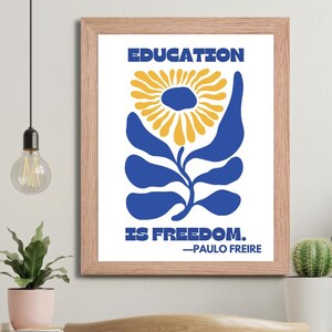 Pu&ograve; includere: Una stampa incorniciata con un design floreale blu e giallo. Il testo "EDUCATION IS FREEDOM." &egrave; stampato sotto il fiore. La citazione &egrave; attribuita a "PAULO FREIRE".