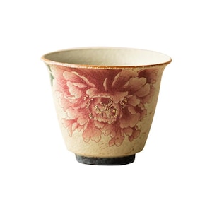 May include: A ceramic teacup with a beige background and a large, detailed red peony floral design. The cup has a slightly flared shape and a dark base. The rim is a darker shade of red.