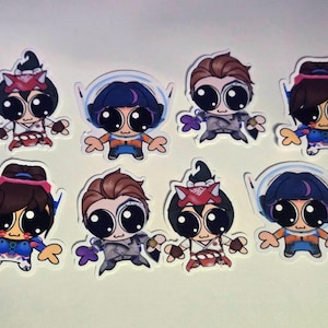 May include: A collection of eight cartoon stickers featuring characters with large eyes and various outfits. The stickers have a white border and are set against a plain background. The characters have different hairstyles and accessories.