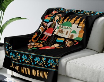 May include: Black fleece throw blanket with a colorful illustration of Ukrainian cultural symbols, including a woman in traditional clothing, a church, and a sunflower. The blanket has a blue and yellow border with the text "Stand with Ukraine".