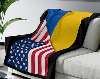 May include: A black fleece throw blanket with the American flag and the Ukrainian flag printed on it. The blanket is draped over a white couch.