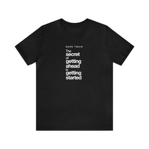 Könnte beinhalten: Schwarzes T-Shirt mit dem Zitat "The secret of getting ahead is getting started" von Mark Twain, weiß gedruckt. Das Shirt hat kurze Ärmel und einen Rundhalsausschnitt.