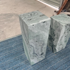 Side profile of a tall green marble pedestal stand with cloudy veining in gray and jade hues. Crafted from natural stone, the rectangular plinth has a clean, modern shape suited for contemporary or gallery-style spaces. Its vertical orientation makes it ideal for displaying plants, sculptures, or floral arrangements. The combination of elegant polish and earthy texture offers a timeless addition to minimalist decor or artistic interiors.