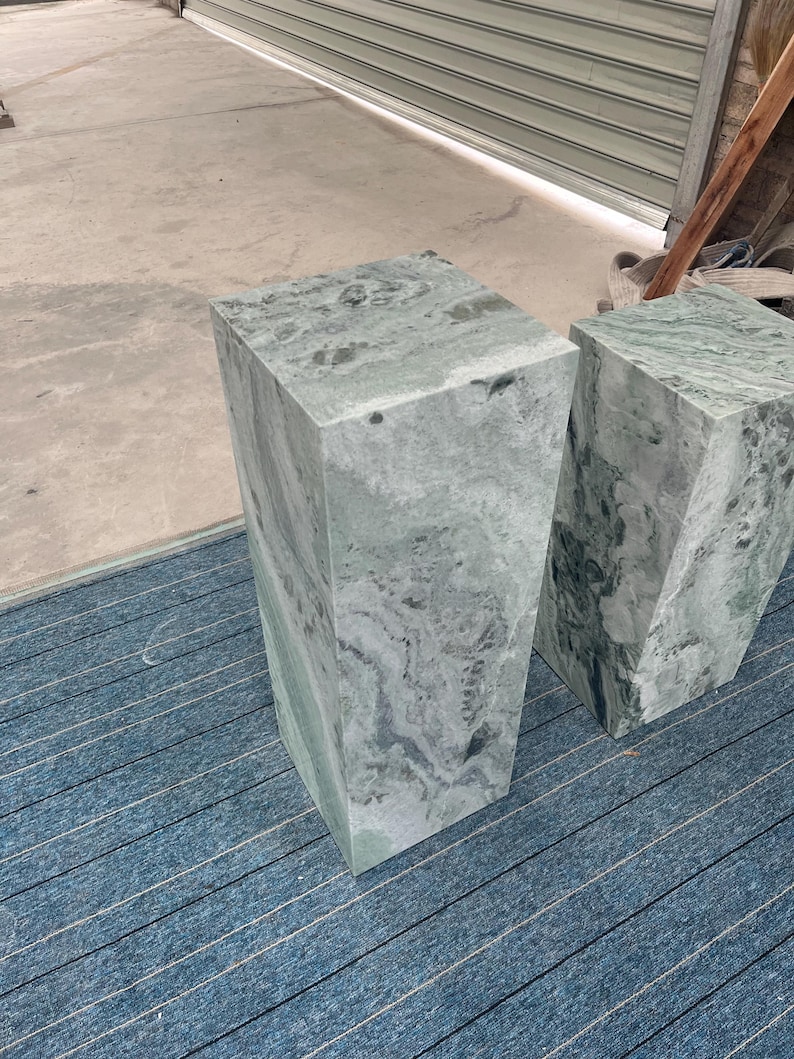 Side profile of a tall green marble pedestal stand with cloudy veining in gray and jade hues. Crafted from natural stone, the rectangular plinth has a clean, modern shape suited for contemporary or gallery-style spaces. Its vertical orientation makes it ideal for displaying plants, sculptures, or floral arrangements. The combination of elegant polish and earthy texture offers a timeless addition to minimalist decor or artistic interiors.