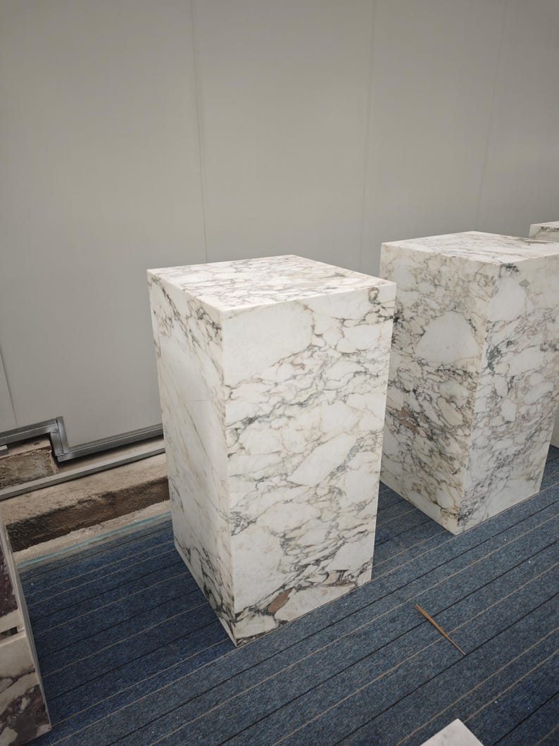 May include: Two white marble pedestals with a gray veining pattern. The pedestals are square and have a smooth, polished surface.