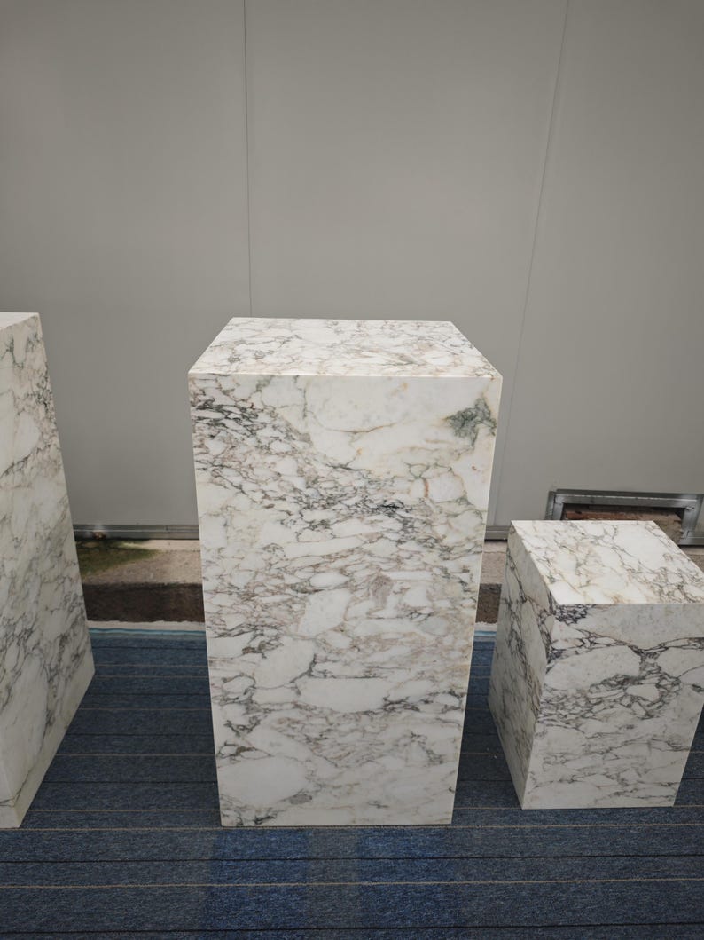 May include: Three white marble pedestals of different sizes. The pedestals are on a blue carpet.