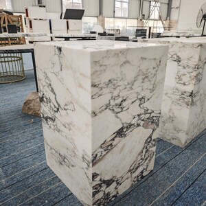 May include: Two white marble pedestals with a gray veining pattern. The pedestals are square and have a smooth, polished surface.