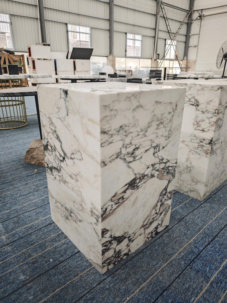 May include: Two white marble pedestals with a gray veining pattern. The pedestals are square and have a smooth, polished surface.