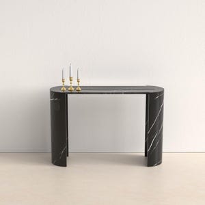 以下が含まれることがあります： 白の縞模様が入った黒大理石のコンソールテーブル。曲線的なデザインで、金色のキャンドルホルダー3つと白いキャンドルが特徴です。テーブルは洗練されたモダンな美学を持っています。