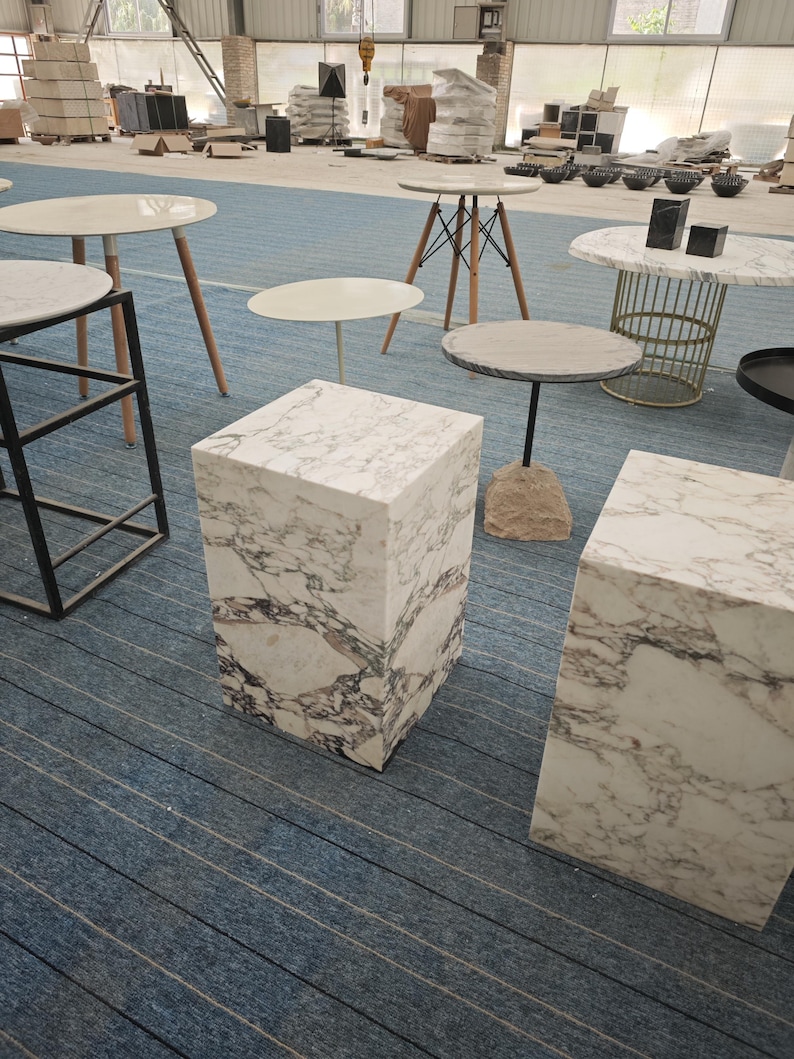 May include: Two white marble square pedestals with gray veining, one on top of the other, on a blue and white striped floor.