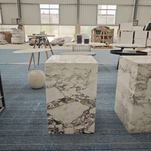 May include: A white marble pedestal table with a white marble top. The table is in a warehouse setting with other furniture.