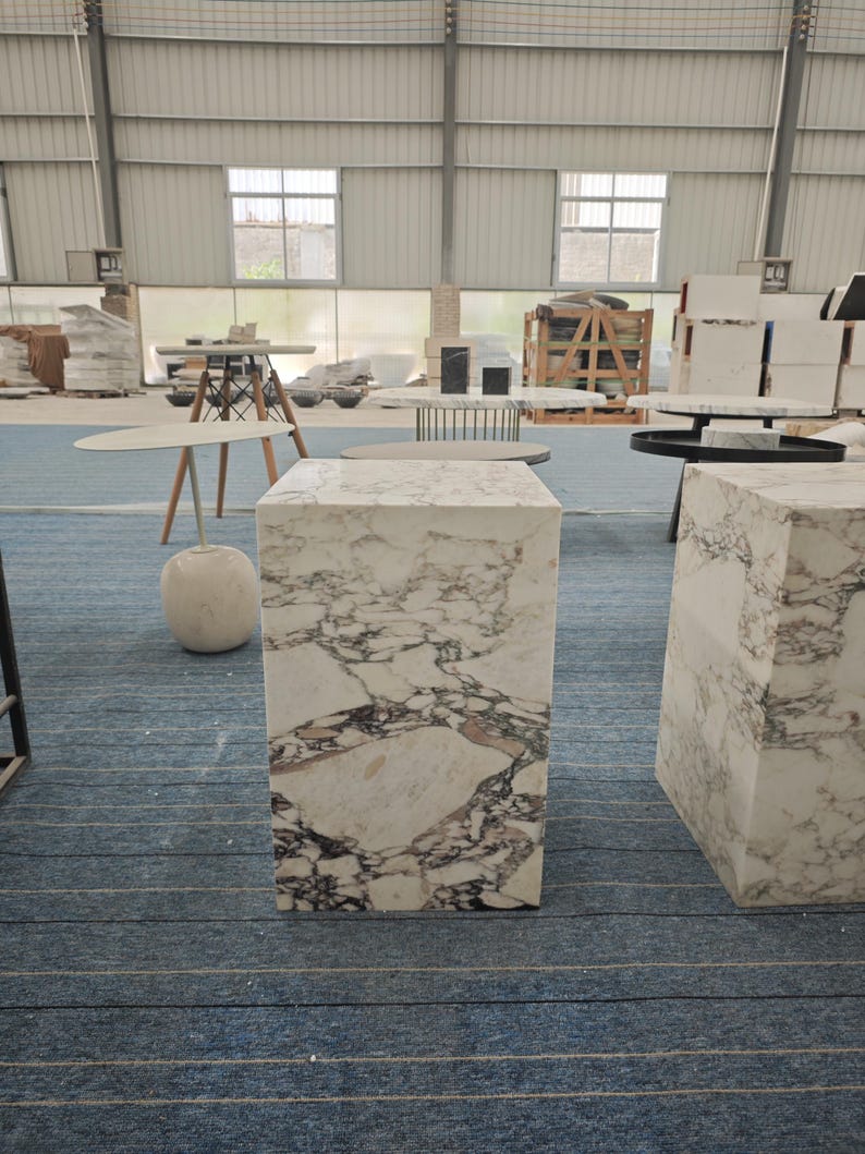 May include: A white marble pedestal table with a white marble top. The table is in a warehouse setting with other furniture.