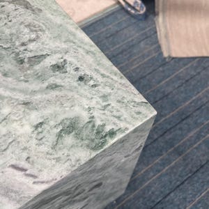 Close-up of a green marble pedestal’s corner showcasing natural veining in light and dark tones. The crisp edge and smooth polish reflect skilled craftsmanship in stone furniture. This detailed view highlights the texture and unique patterning of the marble, offering buyers a sense of the pedestal’s premium quality. Perfect for those looking to add a timeless, sculptural element to modern decor or artistic displays using real natural stone.