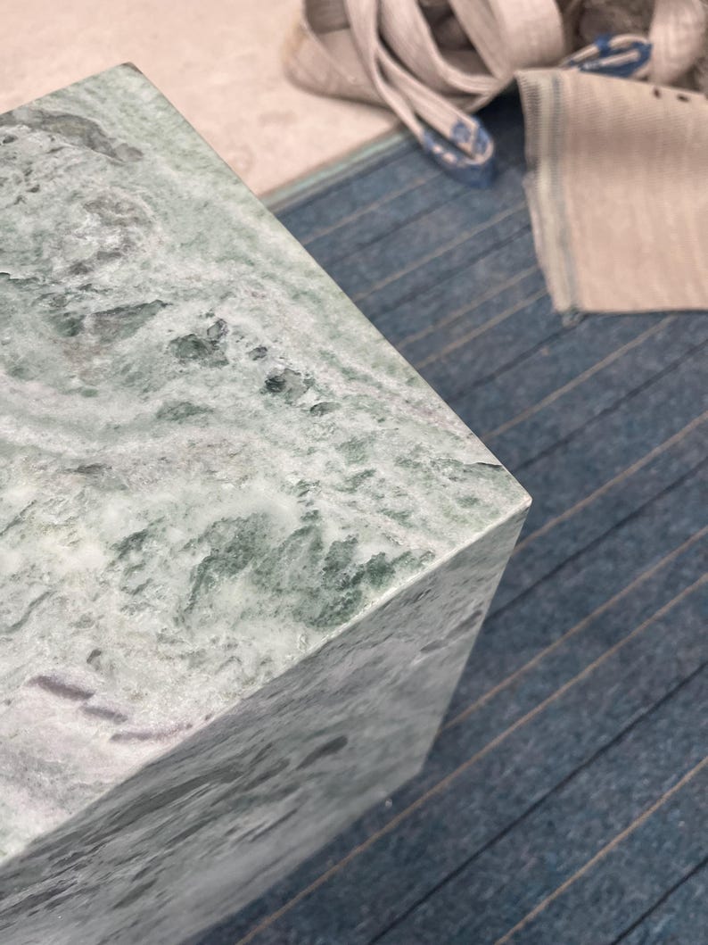 Close-up of a green marble pedestal’s corner showcasing natural veining in light and dark tones. The crisp edge and smooth polish reflect skilled craftsmanship in stone furniture. This detailed view highlights the texture and unique patterning of the marble, offering buyers a sense of the pedestal’s premium quality. Perfect for those looking to add a timeless, sculptural element to modern decor or artistic displays using real natural stone.