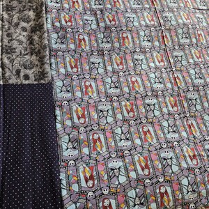 May include: A quilt with a patchwork design featuring a black and white floral pattern, a black fabric with white polka dots, and a colorful fabric with a repeating pattern of Jack Skellington and Sally from The Nightmare Before Christmas.