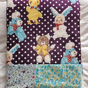 May include: A purple fabric with white polka dots features a variety of stuffed animal designs, including a chick, a bunny, a bear, and a dog. The fabric is sewn together with a patchwork of floral patterns in blue, yellow, and white.