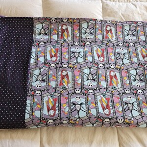 May include: A purple and blue patterned blanket with a black and white polka dot backing. The pattern features a repeating design of Jack Skellington and Sally from the Nightmare Before Christmas.