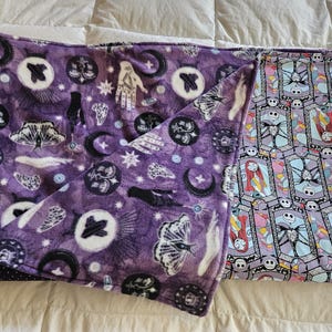 May include: A purple fleece blanket with a black and white pattern of moons, stars, hands, and butterflies. The other side of the blanket is a light purple and blue pattern with a repeated image of a character from the movie The Nightmare Before Christmas.