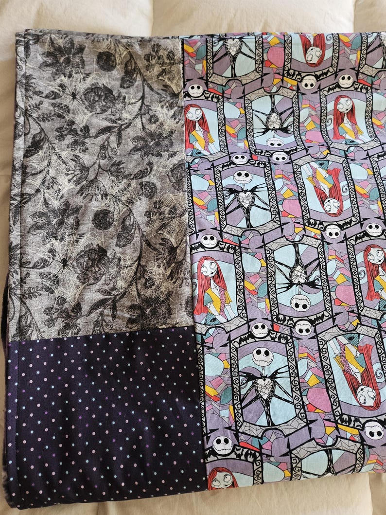 May include: A patchwork quilt with a black and white floral pattern, a black and white polka dot pattern, and a colorful pattern featuring Jack Skellington and Sally from The Nightmare Before Christmas.