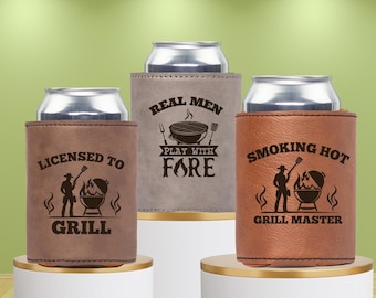 May include: Three brown leather can coolers with different designs. The first cooler says "Licensed to Grill" with a silhouette of a person grilling. The second cooler says "Real Men Play With Fire" with a silhouette of a grill. The third cooler says "Smoking Hot Grill Master" with a silhouette of a person grilling.