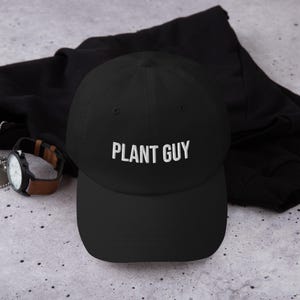 May include: A black baseball cap with white embroidery that reads "PLANT GUY".