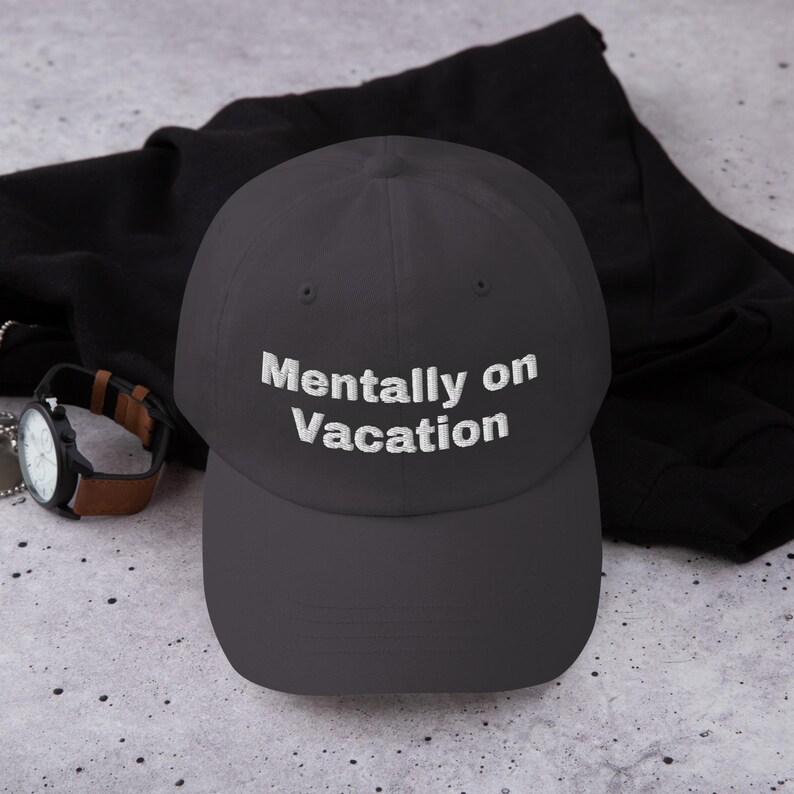 May include: A dark grey baseball cap with white embroidered text that reads "Mentally on Vacation".