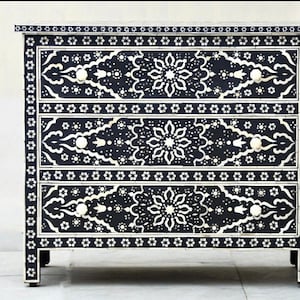 May include: A black chest of drawers with three drawers. Each drawer features a white bone inlay design with intricate floral patterns. The chest of drawers has white bone inlay knobs.