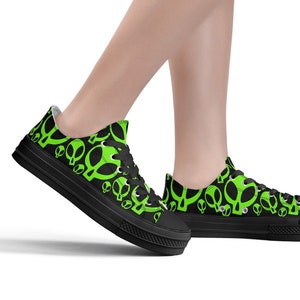 Puede incluir: Zapatillas bajas de lona negras con un patrón de extraterrestres verdes.