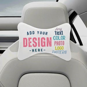 Puede incluir: Coj&iacute;n blanco para reposacabezas de coche con el texto "ADD YOUR DESIGN - HERE-". El texto "DESIGN" es rosa y el resto del texto es azul. El coj&iacute;n est&aacute; en un asiento de coche.
