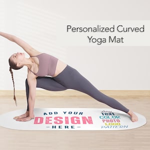 May include: A white, curved yoga mat with the text "Personalized Curved Yoga Mat." The mat has the words "Add Your Design Here" in pink. The mat is oval-shaped and is being used by a person in a yoga pose.