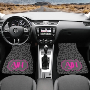 Könnte beinhalten: Zwei schwarze Autofußmatten mit Leopardenmuster. Die Matten haben ein pinkfarbenes Monogramm mit den Initialen "AJH" in einem dekorativen Rahmen.
