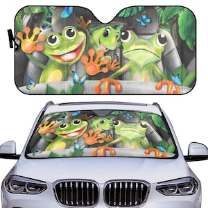 May include: A car sunshade featuring a cartoon image of four green frogs with big eyes and smiles, sitting in a car. The frogs are surrounded by green leaves and butterflies.