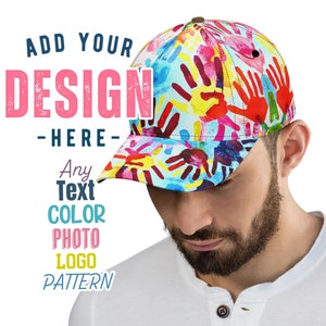 Op de afbeelding: Een baseball cap met een kleurrijk handafdrukontwerp. De cap heeft een gebogen klep en een knoop aan de bovenkant. De tekst "ADD YOUR DESIGN HERE" wordt op de afbeelding weergegeven, samen met andere tekstopties.